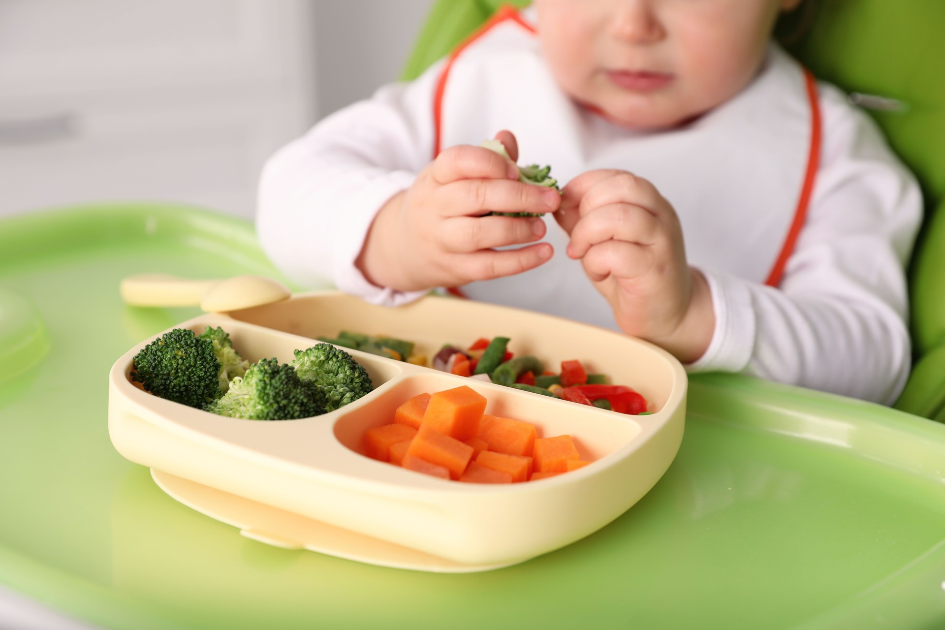Bebê pequeno comendo comida na cadeira alta, close-up